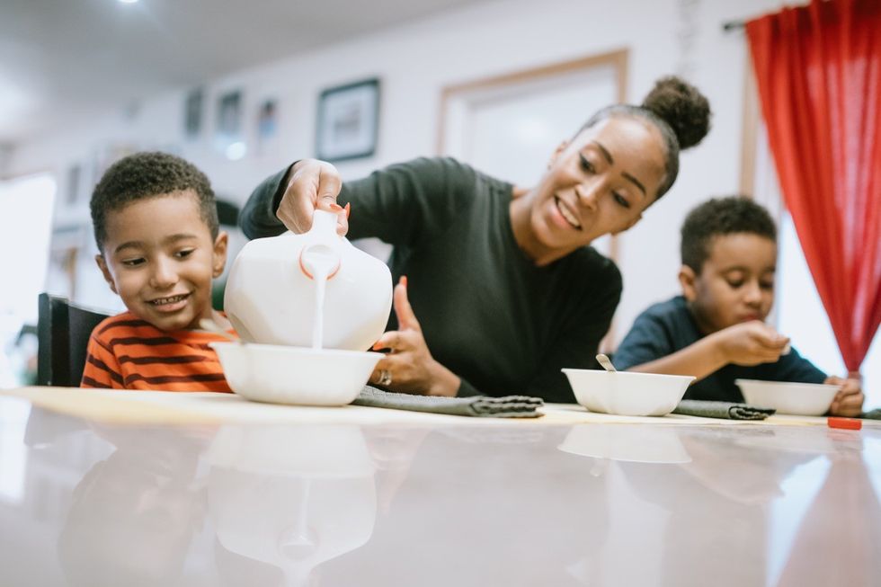 Uma mãe está sentada em casa com os filhos à mesa comendo cereal.