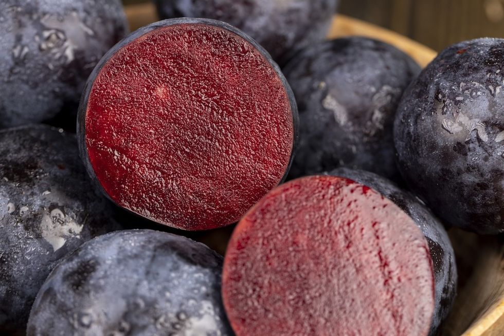 Um close de um corte e uma ameixa inteira